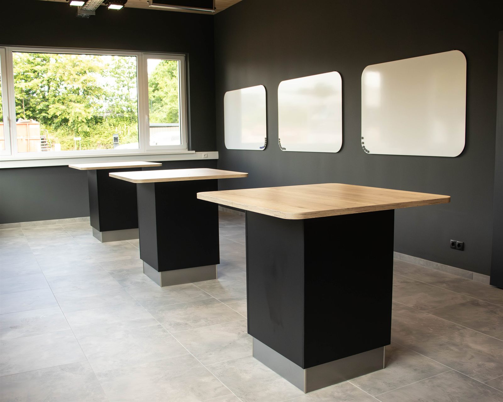 Stehtische vor einer dunklen Wand mit Whiteboards